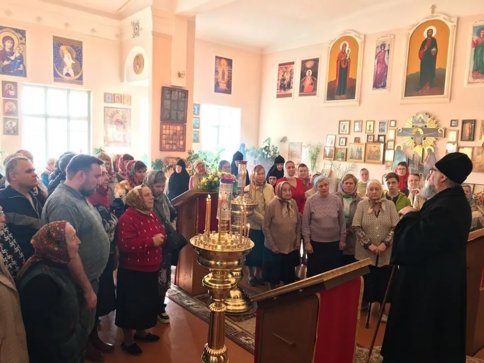 Митрополит и духовенство совершают богослужение в небольшом храме, вокруг — прихожане