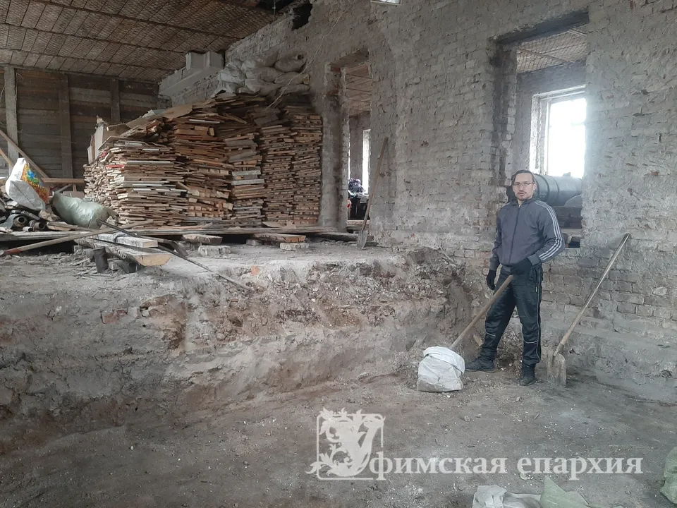 Мужчина стоит среди обгоревших кирпичных стен и досок в пострадавшем от пожара помещении храма